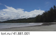 Tropical seascape. The waves of the turquoise ocean roll towards the shore, foaming. The cottages are located in a thicket of green trees on the coast. Clouds in the blue sky. Reflection on wet sand. Стоковое видео, видеограф Вера Ивановна Кубарева / Фотобанк Лори