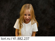 Scowl child 6 year old posing at black, frowning looking at camera. Portrait of angry cover girl kid model in white t-shirt expression emotion, studio shot. Kids emotional concept. Copy ad text space. Стоковое фото, фотограф Aleksandr Golubev / Фотобанк Лори