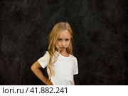 Portrait of angry cover girl kid model in white t-shirt expression emotion, frowning looking at camera, studio shot. Scowl child 6 year old posing at black. Kids emotional concept. Copy ad text space. Стоковое фото, фотограф Aleksandr Golubev / Фотобанк Лори