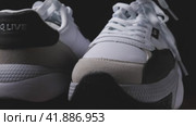 Close-up of two women's white sneakers standing on a wooden surface. Dark background. The camera flies around. Parallax effect. Selective focus. Krasnodar, Russia, April 19, 2022. Редакционное видео, видеограф Воловодов Владимир / Фотобанк Лори