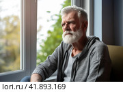 A man sitting at the window of a hospital room, with a sad look. Стоковое AI-изображение, AI-художник Юрий Поздников / Фотобанк Лори