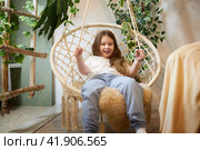 A little girl is relaxing in room with a wicker chair. A schoolgirl is lazy after school. Teen idling at home. Стоковое фото, фотограф Кривошеина Елена Леонидовна / Фотобанк Лори