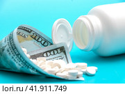 A white jar with pills lies on a blue background. Next to it is a bag made of a hundred dollar bill. Стоковое фото, фотограф Ярославский Максим / Фотобанк Лори