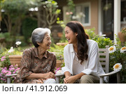 A young Asian girl is talking to her mother in a wheelchair. The concept of caring for the older generation. Стоковое AI-изображение, AI-художник Ярославский Максим / Фотобанк Лори