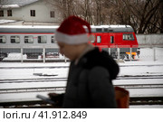 Молодой человек в шапке Санта Клауса идет по перрону в городе Москве, Россия (2023 год). Редакционное фото, фотограф Николай Винокуров / Фотобанк Лори