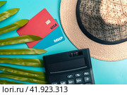 Платежные карты МИР и VISA с соломенной шляпой  и калькулятором на голубом фоне. Концепция отпускных расходов. (2024 год). Редакционное фото, фотограф Ярославский Максим / Фотобанк Лори