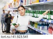 Young girl examining labels on bottles of soju in Asian store. Стоковое фото, фотограф Яков Филимонов / Фотобанк Лори