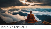 Buddhist monk master is meditating at the top of the cliff at dusk for the new year. Buddhist monk sitting in nirvana on top of mountain above clouds early morning. AI. Стоковое AI-изображение, AI-художник Sergey Grishin / Фотобанк Лори