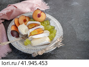Сыр камамбер бри с виноградом и сливами. Камамбер и бри, нарезанные на кусочки. Сыр подается на тарелках ручной работы. Стоковое фото, фотограф Оксана Медведева / Фотобанк Лори