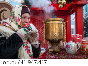 Девушка в русском национальном платке пьет горячий чай во время морозной погоды на мобильной чайной станции в парке города Москвы в рамках фестиваля "Усадьбы Москвы. Зима" в городе Москве, Россия (2024 год). Редакционное фото, фотограф Николай Винокуров / Фотобанк Лори