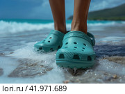 Crocs shod feet of an person on the beach walking along the surf. Стоковое AI-изображение, AI-художник Евгений Харитонов / Фотобанк Лори