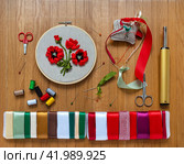 Flat lay of beautiful hand embroidery of red spring poppies with satin ribbons. Accessories: needles, pins, threads, red and green satin ribbons and lighter for processing satin cuts on wooden table. DIY concept. Copy space, top view, closeup, mock up. Стоковое фото, фотограф Виктория Катьянова / Фотобанк Лори