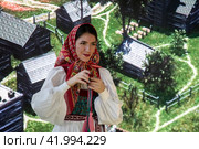 Девушка в русской народной одежде скручивает тесьму со славянским орнаментом на стенде Орловской области  во время проведения выставки-форума "Россия" на ВДНХ в городе Москве, Россия (2024 год). Редакционное фото, фотограф Николай Винокуров / Фотобанк Лори