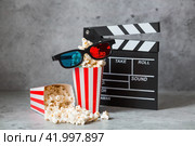 A banner for the film industry. A movie date. A movie camera, 3D glasses, popcorn in striped cups on a stylish concrete gray background. The premiere of the film. (2024 год). Стоковое фото, фотограф Photojuli / Фотобанк Лори