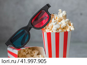 A banner for the film industry. The release date of the film. 3D glasses and popcorn in striped cups on a stylish concrete-gray background. The premiere of the film. (2024 год). Стоковое фото, фотограф Photojuli / Фотобанк Лори