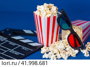 A banner for the film industry. A romantic movie date. A movie camera, 3D glasses, popcorn in striped cups on a blue background. The premiere of the film. (2024 год). Стоковое фото, фотограф Photojuli / Фотобанк Лори