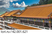 The tiled roofs of Chinese houses are elegantly curved and decorated with ornaments. The terraces are fenced with railings. A green hill against a sky and clouds. Malaysia. Penang. Kek Lok Si Temple (2023 год). Стоковое фото, фотограф Вера Ивановна Кубарева / Фотобанк Лори