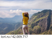Rear view of adult woman enjoying at landscape Adam's peak mountain in tropical journey Sri Lanka, Ella. From behind of lady in yellow jacket posing at landmark nature background. Copy ad text space (2022 год). Стоковое фото, фотограф Aleksandr Golubev / Фотобанк Лори