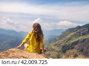 Rear view of lady in yellow jacket sitting at landmark nature background, Sri Lanka, Ella. From behind of woman enjoy at landscape Adam's peak mountain. Summer vacation concept. Copy ad text space. Стоковое фото, фотограф Aleksandr Golubev / Фотобанк Лори