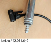 Sports tools: old aluminum hand pump with an attached ball's needle adapter, placed above the black hose. Compact metal pump with tiny scratches on its surfaces and a plastic adapter for bike' nipples. Стоковое фото, фотограф Анатолий Власов / Фотобанк Лори
