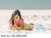Happy cute smiling little girl in sunglasses lying on the sand on a beach in a swimsuit. Summer concept. Стоковое фото, фотограф Ирина Михайличенко / Фотобанк Лори