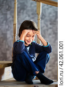 Fake tears of little boy, 7 years old, of European appearance, sitting on step of wooden staircase in private two story house. Стоковое фото, фотограф Владимир Григорьев / Фотобанк Лори