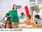 Female teacher, conducting extracurricular lesson in the school class tells schoolchildren the history of Mexico and shows national flag of country. Стоковое фото, фотограф Яков Филимонов / Фотобанк Лори