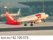 Самолет Сухой SuperJet 100-95LR авиакомпании Red Wings взлетает на фоне терминала аэропорта Пулково (2021 год). Редакционное фото, фотограф Сергей Крамарев / Фотобанк Лори
