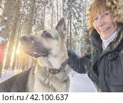 Adult girl with shepherd dog taking selfies in a winter forest. Middle aged woman and big shepherd dog on nature in cold day. Friendship, love, communication, fun, hugs. Стоковое фото, фотограф Кривошеина Елена Леонидовна / Фотобанк Лори