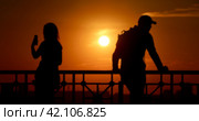 A blurred photograph of two people silhouettes a man and a woman at sunset in the city. A woman takes a selfie, a man in a cap looks away. Стоковое фото, фотограф Валерий Леонидович / Фотобанк Лори