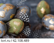 Stylish beautiful Easter eggs with a golden coating of sweat and feathers in a bird's nest of brushwood on a gray background. The concept of happy Easter 2024. Стоковое фото, фотограф Photojuli / Фотобанк Лори