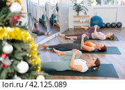 Girl performing Ardha Pawanmuktasana during training in Christmas yoga studio. Стоковое фото, фотограф Яков Филимонов / Фотобанк Лори