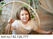 A little girl is relaxing in room with a wicker chair. A schoolgirl is lazy after school. Teen idling at home. Стоковое фото, фотограф Кривошеина Елена Леонидовна / Фотобанк Лори