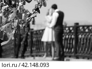 MoA couple in love in blurred focus stands on a bridge and kisses. Moscow, Love Bridge or Tretyakov Bridge. It is black the white photo. Stands a tree with metal locks of lovers (2016 год). Редакционное фото, фотограф Валерий Леонидович / Фотобанк Лори