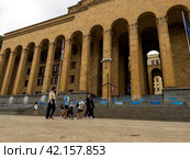 A young family with children walk along the street past the Georgian Parliament building on Shota Rustaveli Avenue. Tbilisi. Georgia. 03.09.2023. Редакционное фото, фотограф Ярославский Максим / Фотобанк Лори