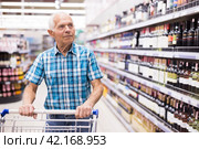 Elderly retired senor buying wine in the alcohol section of the supermarket. Стоковое фото, фотограф Татьяна Яцевич / Фотобанк Лори