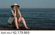 Young adult blonde sitting on log on beach on background of ocean waves. Cinematic shot. Стоковое видео, видеограф А. А. Пирагис / Фотобанк Лори