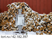 Traditional Russian samovar. A classic metal samovar against the background of a stack of firewood. Tea tradition in a village in Russia. Rural lifestyle. Nostalgic mood. Winter in the countryside. Стоковое фото, фотограф Андрей Степанов / Фотобанк Лори