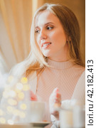 Beautiful young woman is drinking coffee. Attractive woman in a cozy cafe. Pretty woman in a white sweater warms her hands near a cup of hot cappuccino. Close-up. Shallow depth of field. Soft focus. Стоковое фото, фотограф Андрей Степанов / Фотобанк Лори