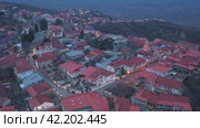 Scenic view from drone of Signagi township with narrow winding streets and brownish roofs on steep hill in foothills of Gombori Range in spring twilight, Georgia. Стоковое видео, видеограф Яков Филимонов / Фотобанк Лори