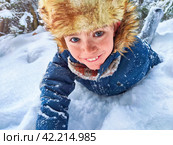 Disabled boy without an arm crawls through the snow while playing snowballs in winter in a snowdrift. The suffering of civilians in the war and confrontation between Ukraine and Russia. Стоковое фото, фотограф Кривошеина Елена Леонидовна / Фотобанк Лори