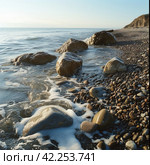 Rocks and pebbles are softly caressed by the ebbing and flowing tide. Стоковое AI-изображение, AI-художник Юлия Гапеенко / Фотобанк Лори