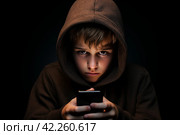 A boy in a hoodie is coolly looking at a mobile phone in the darkness. Стоковое AI-изображение, AI-художник Igor Bastrakov / Фотобанк Лори