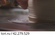A potter working a clay jug on a potter's wheel with a special tool. A close-up view. A potter is practising pottery, handicraft, working with clay. Slow motion. Стоковое видео, видеограф Воловодов Владимир / Фотобанк Лори