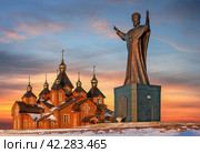 Памятник Святителю Николаю Чудотворцу и Кафедральный собор Святой Живоначальной Троицы, город Анадырь, Чукотка, Россия. Живописный вид на деревянную православную церковь и памятник Святителю Николаю Чудотворцу. Красивое небо. Христианство в Сибири и на Дальнем Востоке России. Редакционное фото, фотограф Андрей Степанов / Фотобанк Лори