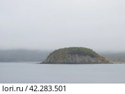 Вид на небольшой остров в морской бухте. Осенний морской пейзаж. Пасмурная погода. Низкие облака. Природа Дальнего Востока России. Остров Вдовушка, бухта Весёлая, Охотское море, Магаданская область, Россия. Стоковое фото, фотограф Андрей Степанов / Фотобанк Лори