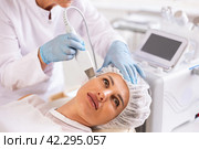 Young female client experiencing facial skin peeling with ultrasonic scrubber. Стоковое фото, фотограф Яков Филимонов / Фотобанк Лори