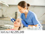 Experienced cosmetologist in rubber gloves does rf-lifting procedure on face for girl, smoothes wrinkles and tightens skin with use of electric hydrogen oxygen facial beauty machine in spa center. Стоковое фото, фотограф Яков Филимонов / Фотобанк Лори