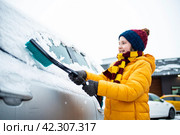 мальчик помогает родителям убрать снег с лобового стекла машины, очистить окно автомобиля зимой от снега зимой. Стоковое фото, фотограф Яна Проничева / Фотобанк Лори