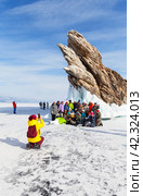 BAIKAL LAKE, KURKUT VILLAGE, IRKUTSK REGION, RUSSIA -  March 02, 2024: Group of tourists traveling on ice of frozen Baikal Lake take souvenir photos near famous icy Dragon Cape of Ogoy Island. Редакционное фото, фотограф Виктория Катьянова / Фотобанк Лори